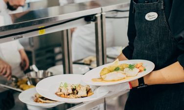 Tarjoilijaopiskelija nostaa kolme erillistä annosta samanaikaisesti käsiinsä Stadin AO:n ravintola Kokissa.