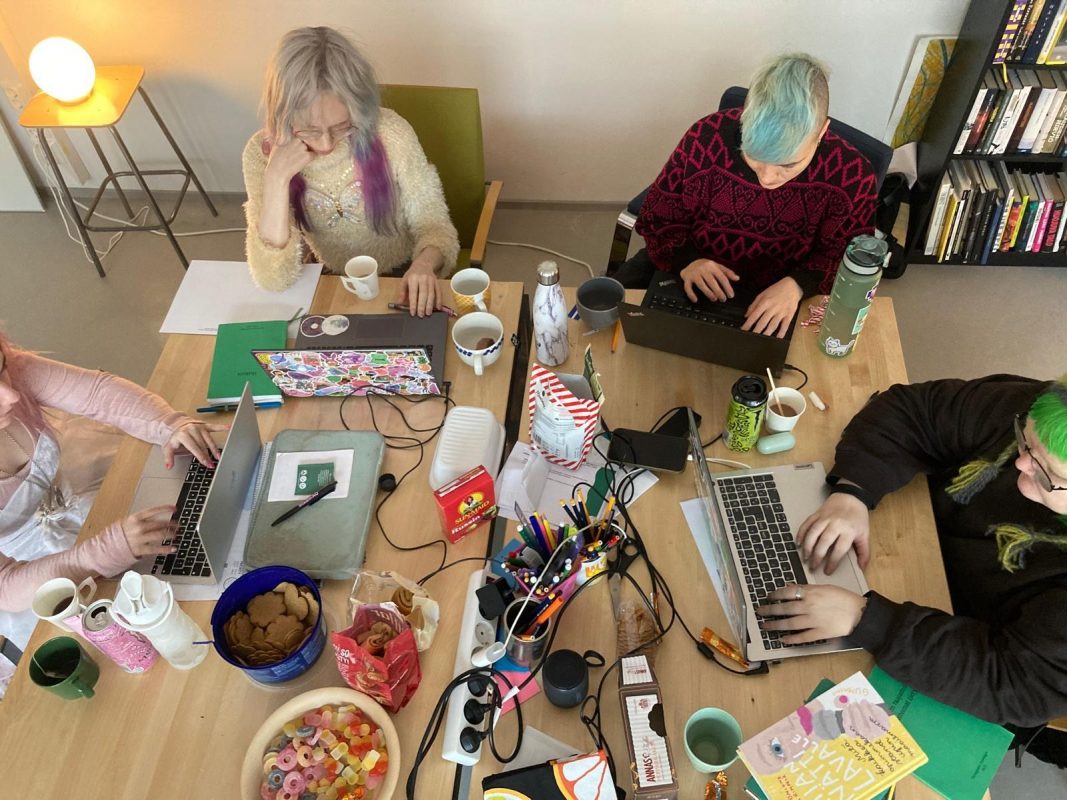 Nuoria työkokeilijoita kirjoitusvälineiden koristaman pöydän ympärillä.  